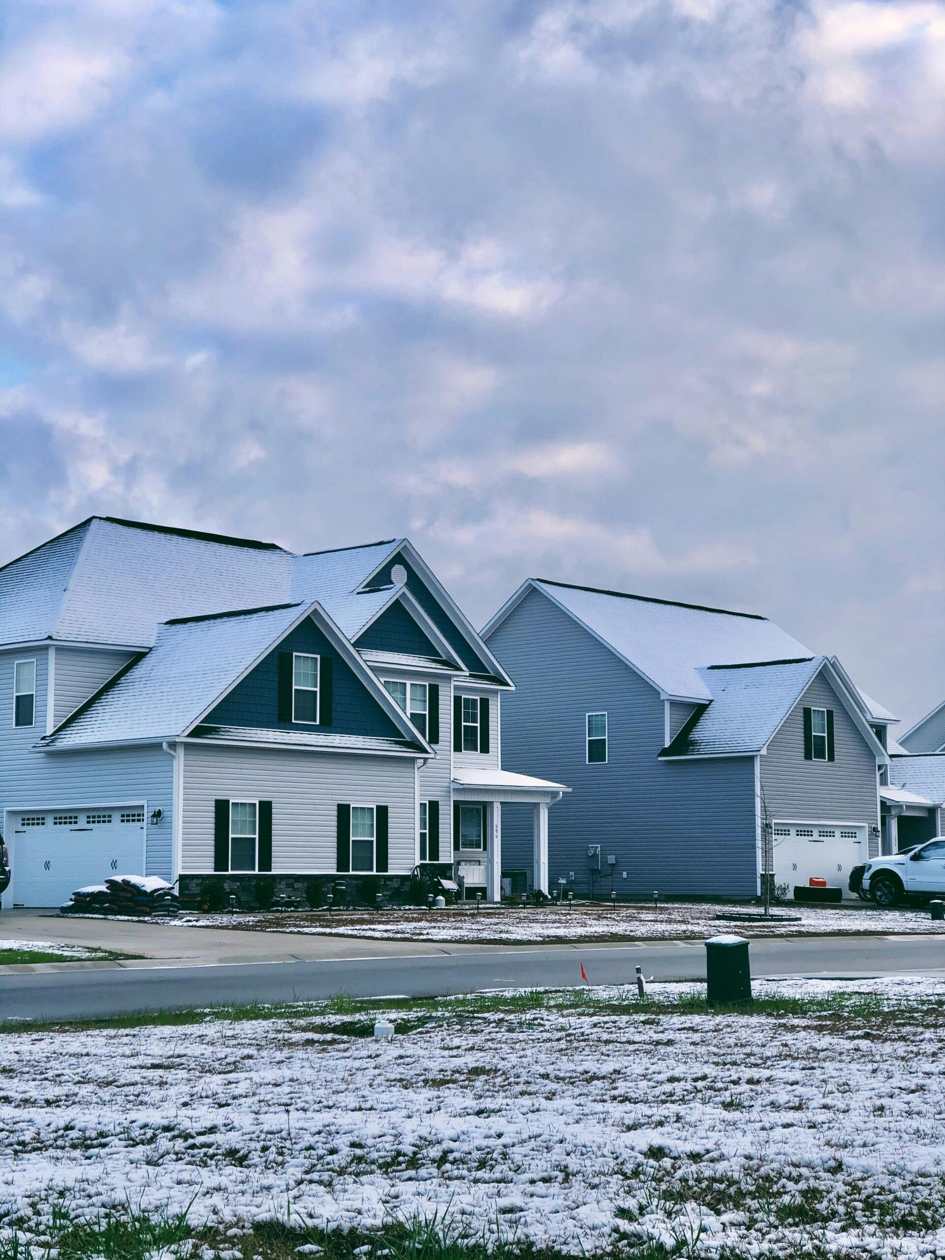 Charming suburban homes with light snow on rooftops and ground, cloudy winter sky overhead.
